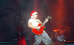 A man in a santa claus outfit playing a guitar.