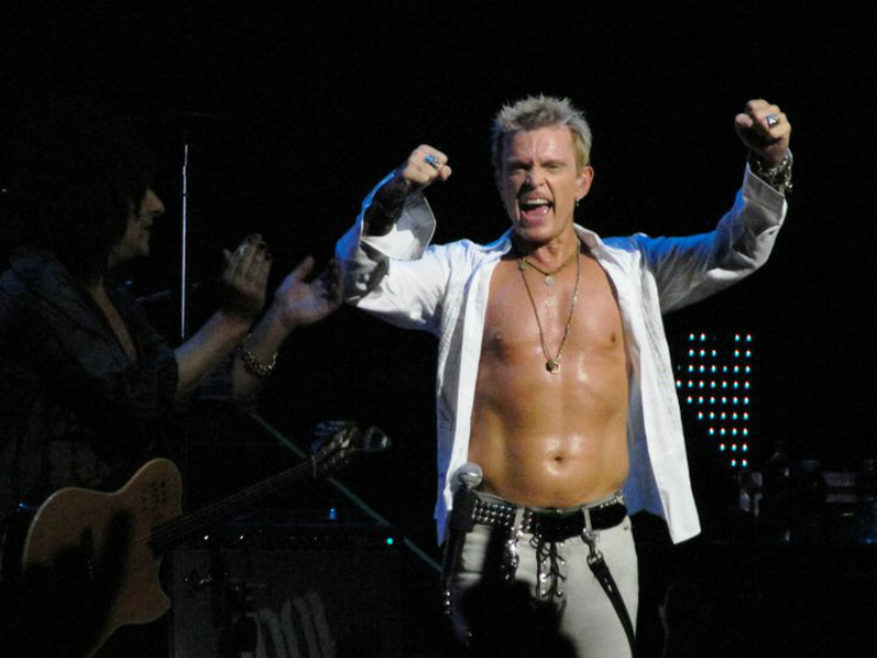 A shirtless man with his arms up on stage.