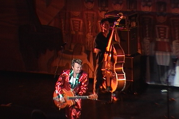 A man in a red suit playing a guitar on stage.