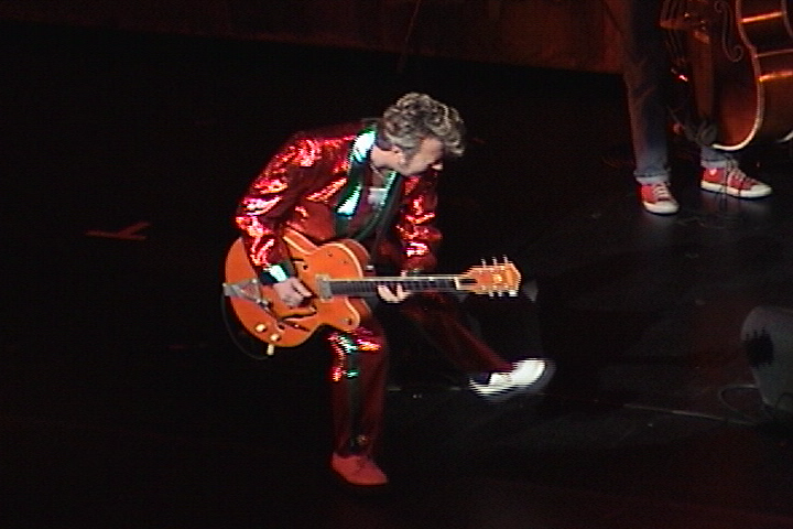 A man in a red suit playing a guitar.