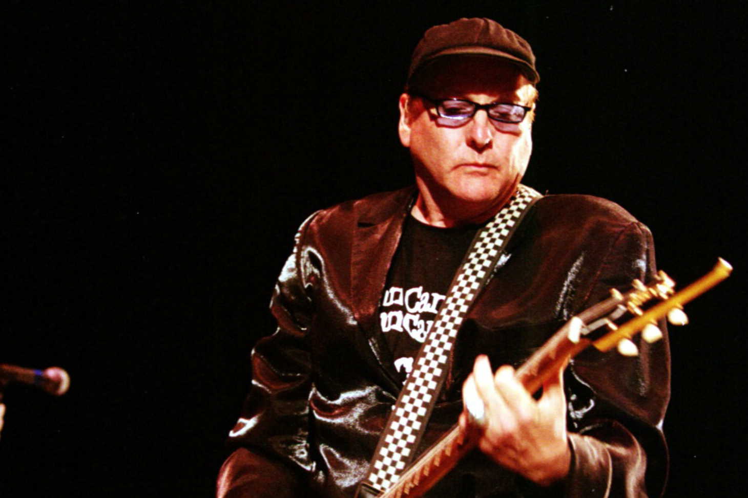 A man in a black jacket playing a guitar.