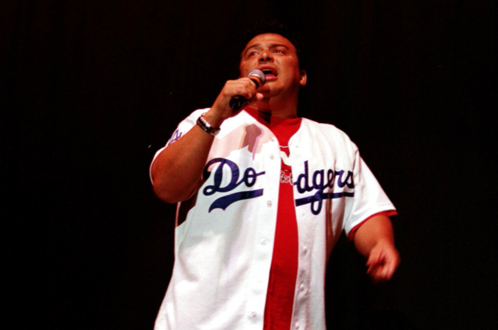 A man in a dodgers jersey singing into a microphone.