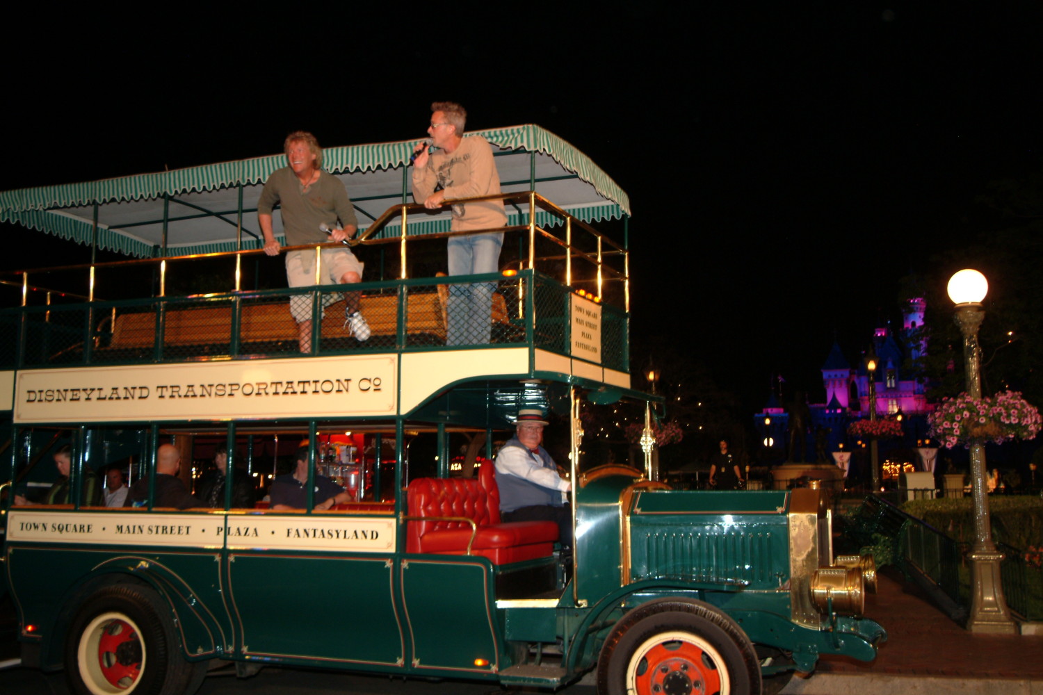 A green double decker bus with people on top.