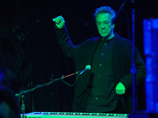 A man in a black jacket standing in front of a keyboard.