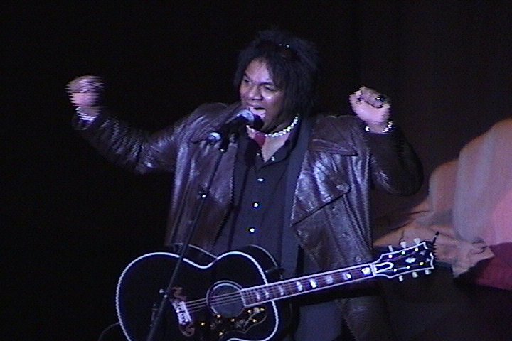 A man in a leather jacket holding an acoustic guitar.