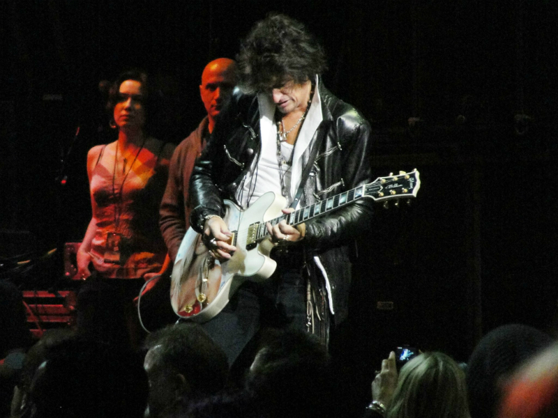 A man in a leather jacket playing a guitar in front of a crowd.