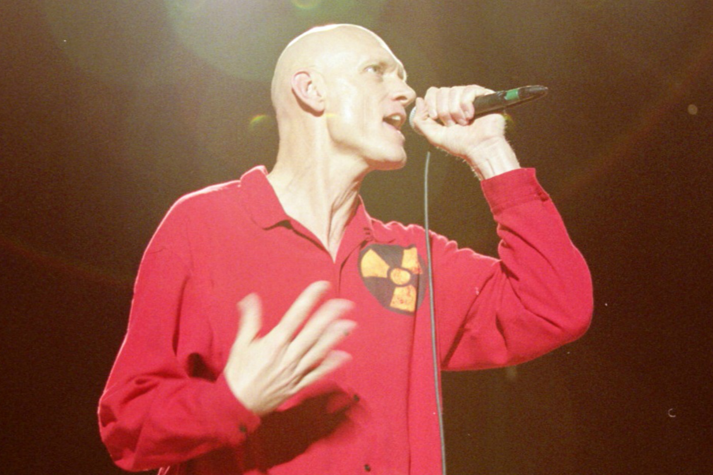 A bald man in a red shirt singing into a microphone.