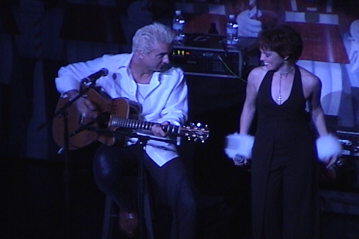 A man and a woman singing and playing an acoustic guitar.