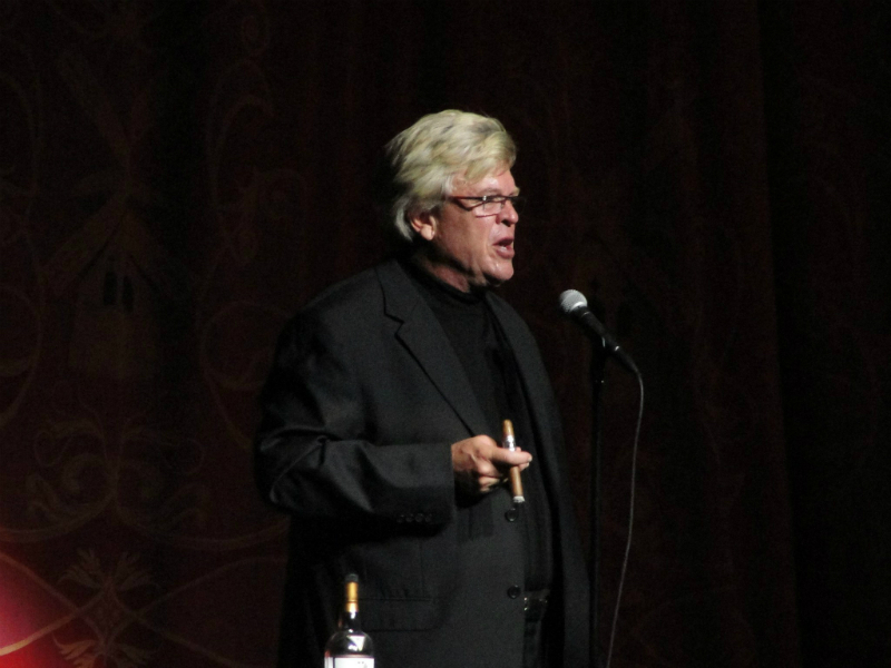 A man in a black suit is speaking into a microphone.