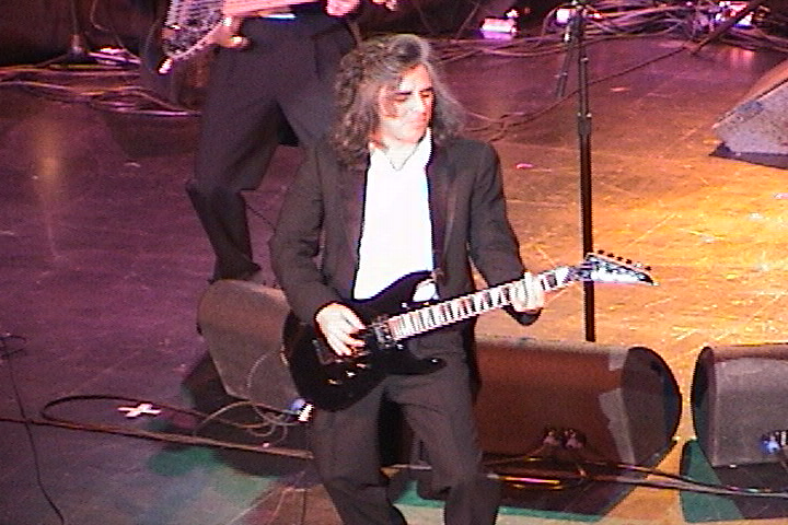 A man in a suit playing a guitar on stage.