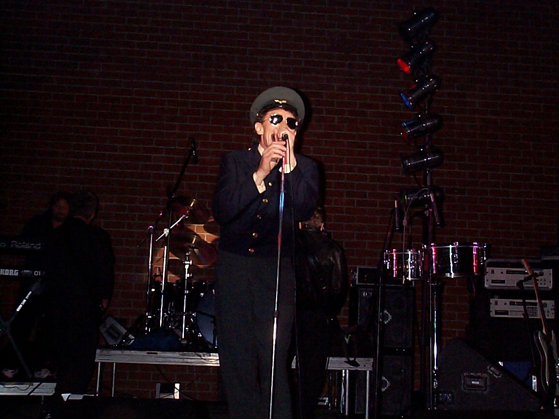 A man in black jacket holding microphone on stage.