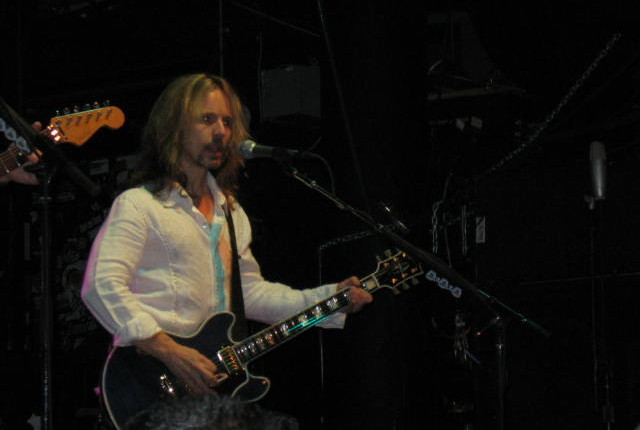 A man in white shirt playing guitar on stage.