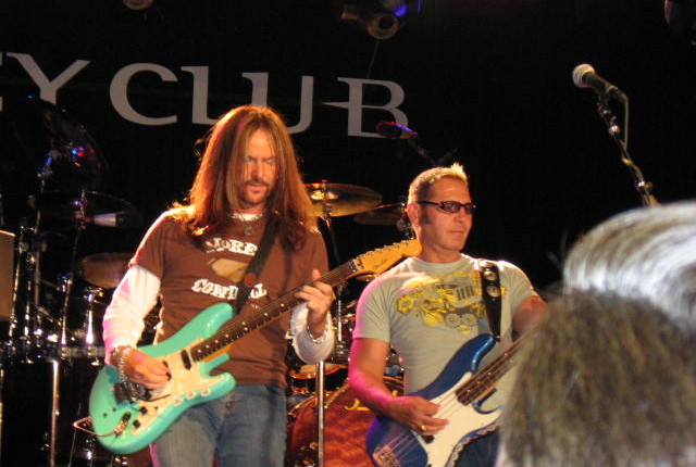 Two men playing guitar and drums on a stage.
