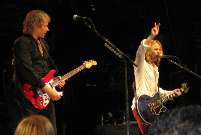 A man with a guitar and another man on stage