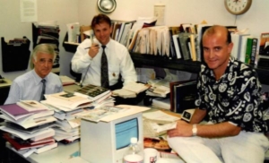 Two men sitting at a desk with papers on the table.