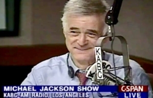A man in a blue shirt and tie sitting at a radio station.